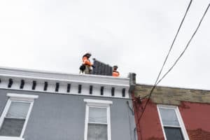 Two solar panel technicians moving a solar panel atop of a residential building