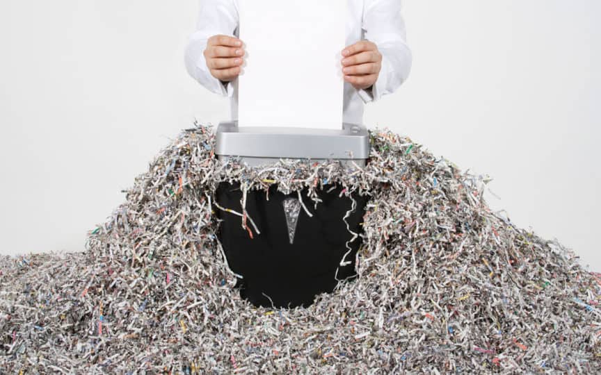 Paper shredder over a trash bin with paper shreds overflowing