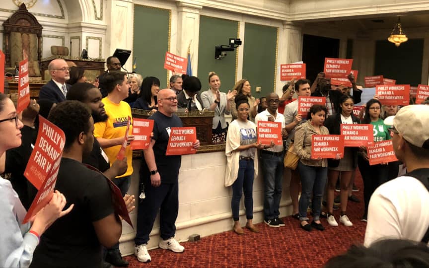 Councilmember Helen Gym and community members in Council chambers hold signs that read Philly workers demand a fair workweek