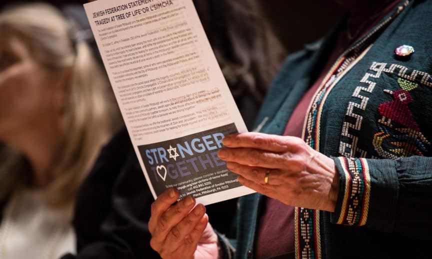 Close up of woman's hands holding a flyer from the Jewish Federation, commemorating the Tree of Life victims