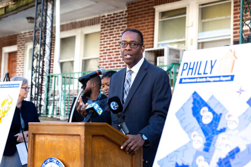 Council President Darrell Clarke speaks at a podium in front of housing with map posters on either side of him