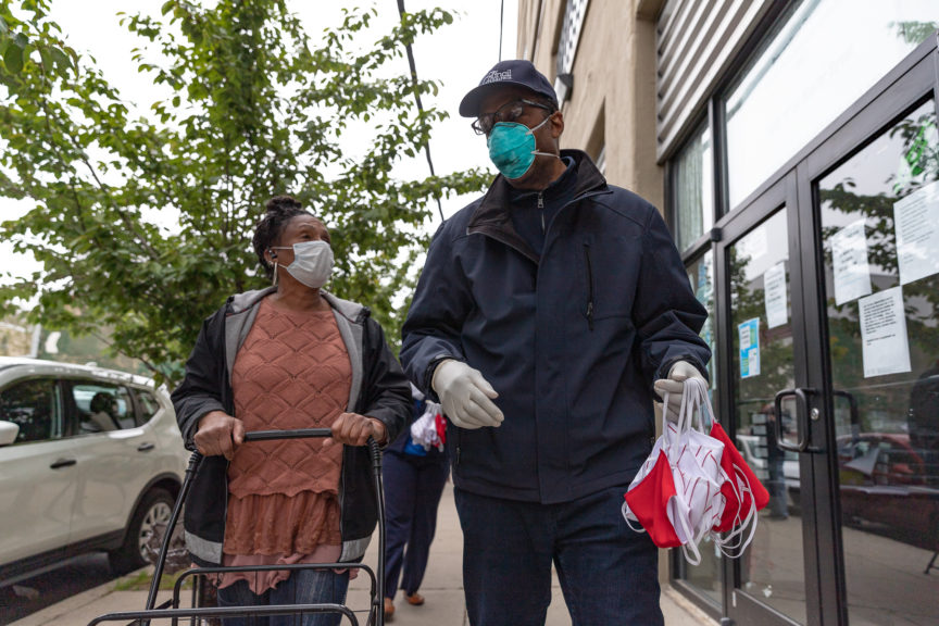 Darrel Clarke with a handful of masks, walking next to and speaking with an unknown woman.